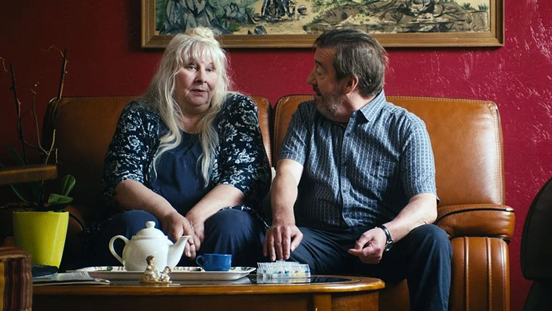 Yolande Moreau et Bruno Lochet assis l'un à côté de l'autre dans un canapé face à un service à thé.