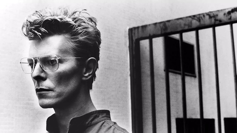 David Bowie par Helmut Newton, 1982. Bowie se tient de profil et porte des lunettes de vue. Son visage est inexpressif, il semble regarder dans le vide. Mais surtout, ses traits son très anguleux.