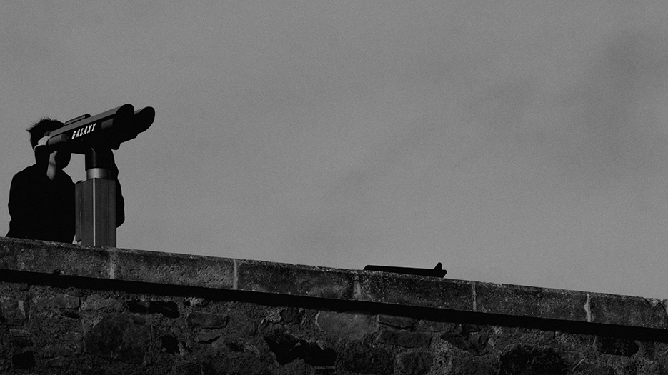 Photo en noir et blanc d'un jeune garçon qui regarde au loin avec un télescope de bord de mer.