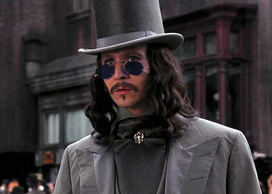 Gary Oldman dans Dracula, habillé à la mode victorienne : costume gris, chapeau haut-de-forme, lunettes de soleil steampunk et cheveux longs avec des boucles bien dessinées.