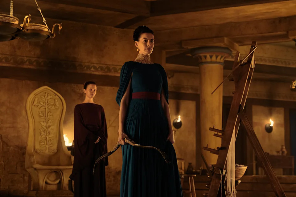 Pénélope, jouée par Anne Hathaway, tenant l'arc d'Ulysse dans la main, face à ses prétendants.