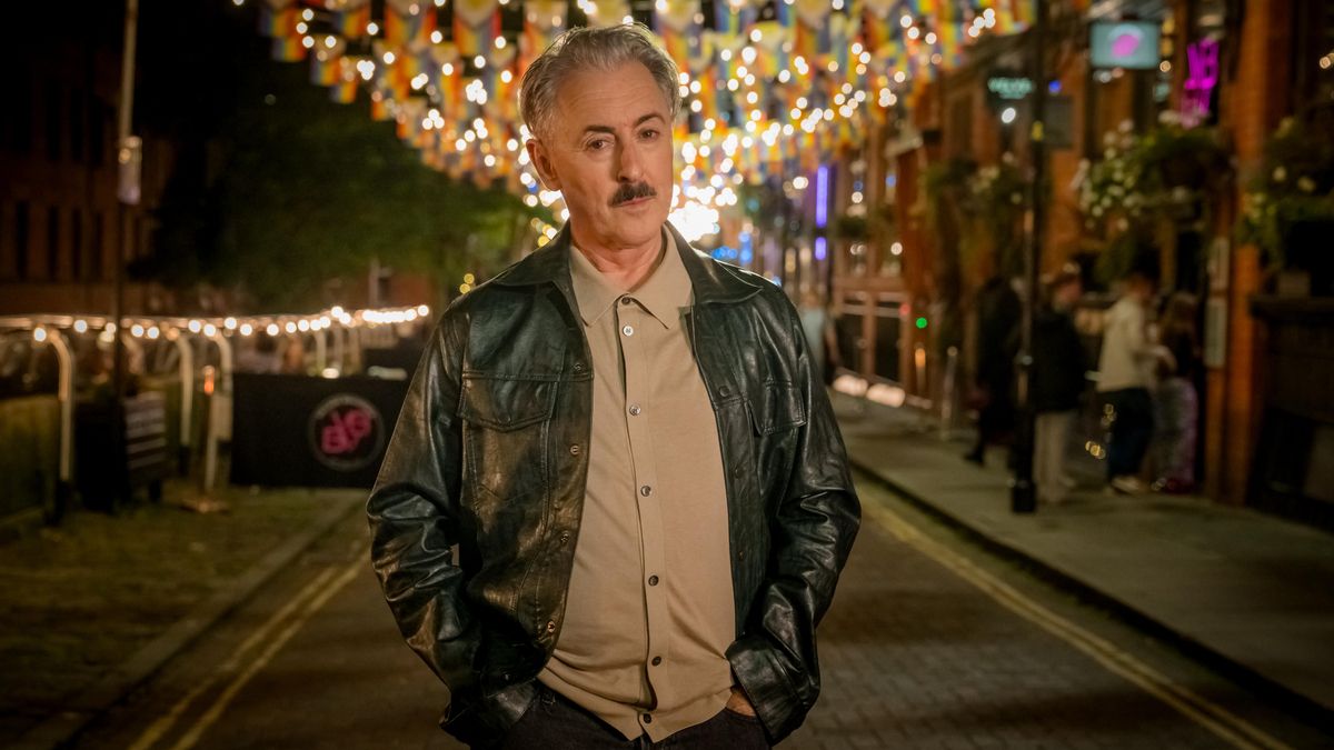 Alan Cumming dans le rôle de Leo. Il arrive à 60 ans, porte les cheveux courts et gris, ainsi qu'une petite moustache noire. Il porte une veste en cuir par-dessus un polo beige.